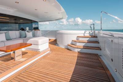 A luxurious yacht deck with comfortable seating, a hot tub, and a wooden floor, set against a backdrop of a clear blue sky and calm waters.
