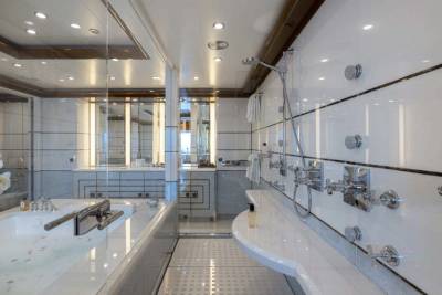 A modern, well-lit bathroom with a large bathtub, multiple showerheads, and a sleek, minimalist design featuring white tiles and wooden accents.