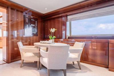 A luxurious and modern dining room with a wooden paneled interior, a large window offering a scenic view, and a round dining table with plush chairs.