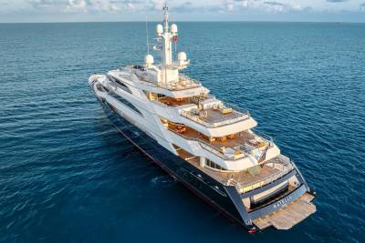 A massive, luxurious yacht sits atop the serene, azure waters, surrounded by a picturesque ocean backdrop with a cloudy sky.