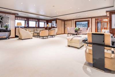 A spacious and elegantly furnished living room with wooden accents, plush seating, and a modern fireplace, overlooking a scenic outdoor view through large windows.