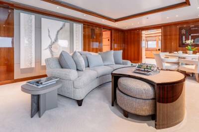 A luxurious and well-appointed living room with plush gray sofas, a round wooden coffee table, and a dining area with a white table and chairs, all set against a backdrop of warm wood paneling and artwork on the walls.