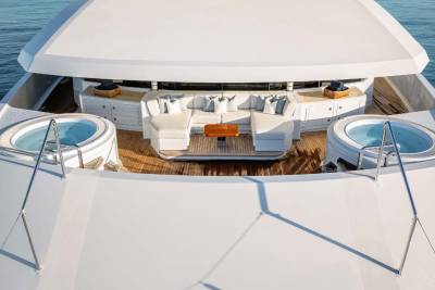 A white yacht with a spacious deck and seating area, surrounded by the serene blue waters of the ocean.
