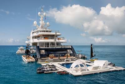 A large, luxurious yacht is anchored in the middle of a vibrant blue ocean, surrounded by fluffy white clouds in the sky.