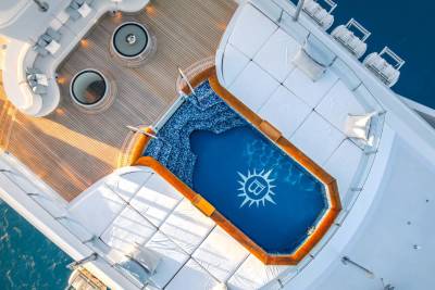 A vibrant blue swimming pool surrounded by a white and orange cruise ship structure, with speakers and other equipment visible in the foreground.