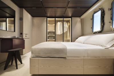 A luxurious yacht cabin features a plush bed, elegant closet, and porthole windows offering a glimpse of the sea.