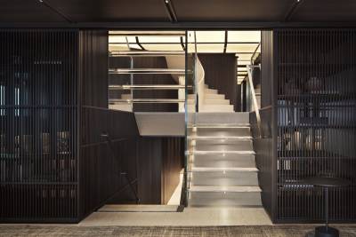 A modern staircase with glass railings and integrated lighting ascends through a stylish, dark wood interior.