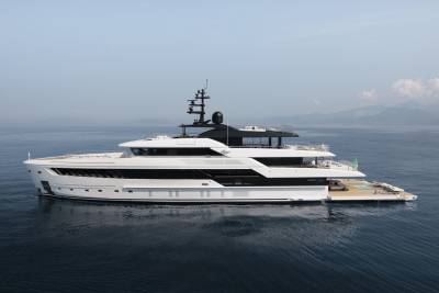 A sleek white superyacht glides through calm blue waters with a backdrop of hazy mountains.
