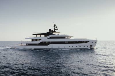 A sleek white superyacht glides through the deep blue ocean under a clear sky.