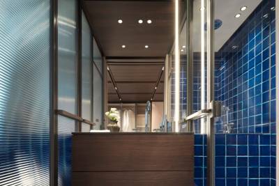 A modern bathroom features a dark wood vanity, blue tiled shower, and ribbed glass partitions.