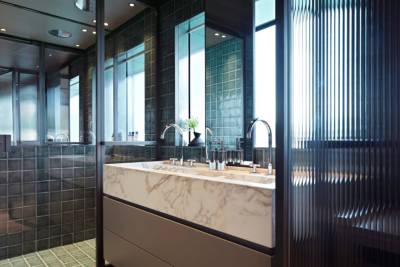 A modern bathroom features a marble double vanity with sleek chrome fixtures and a fluted glass partition.