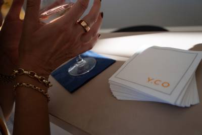 A hand adorned with a ring and bracelets holds a glass of rosé over a dark blue coaster next to a stack of white napkins.