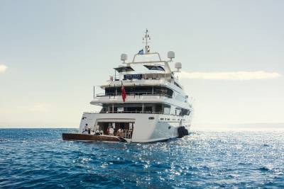 A luxurious superyacht glides across the sparkling blue ocean under a clear sky.
