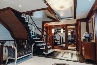 Luxurious wood and marble finishes adorn this elegant yacht interior, featuring a grand staircase and opulent seating.