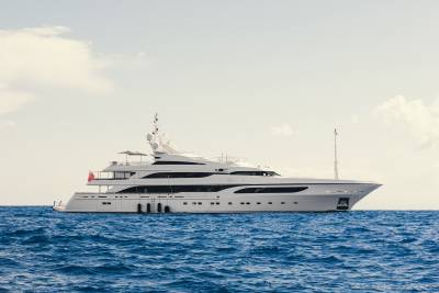 A luxurious white yacht glides across the deep blue ocean under a hazy sky.