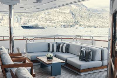 Relax on the plush outdoor seating of this luxurious yacht while admiring the stunning coastal city and mountainous backdrop.