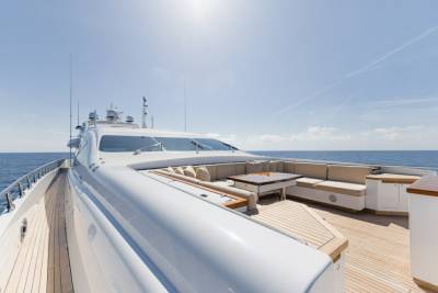 A luxurious yacht deck offers ample seating and a dining table for enjoying the serene ocean views under a clear blue sky.