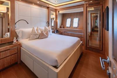Luxurious yacht accommodations feature a plush bed, elegant wood finishes, and porthole windows offering a glimpse of the sea.