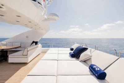 Luxurious white cushions and plush navy pillows invite relaxation on the sun-drenched deck of a yacht overlooking the tranquil blue sea.