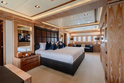 Luxurious master suite aboard a yacht features a king-sized bed, rich wood paneling, and a private seating area.