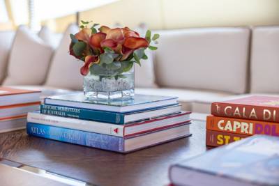 A vase of burnt orange calla lilies rests on a stack of coffee table books on a wooden table.