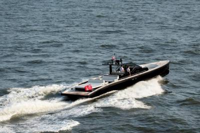 A sleek black yacht cuts through the choppy blue water, leaving a foamy white wake in its path.