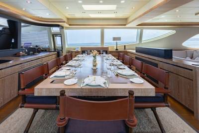A long, elegant dining table is set for a formal meal aboard a luxurious yacht with expansive ocean views.