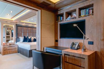 A modern yacht cabin features a sleek desk and entertainment center adjacent to a luxurious bedroom.