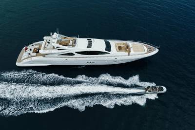 A sleek white yacht cruises through the deep blue ocean, leaving a foamy wake behind it as a smaller boat follows.