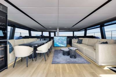 A modern and stylish interior of a boat or yacht, featuring comfortable seating arrangements, a dining area, and large windows providing a panoramic view of the surrounding environment.