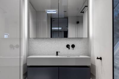 A modern, minimalist bathroom with a white sink, black fixtures, and a large mirrored cabinet against a tiled wall.