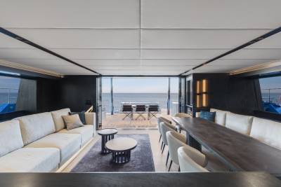 A modern and minimalist living room with large windows overlooking a scenic outdoor view, featuring a plush sectional sofa, a wooden dining table, and various decorative elements.