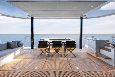 A spacious outdoor deck with a panoramic view of the ocean, featuring a seating area with chairs and a table, surrounded by a glass enclosure that provides shelter from the elements.