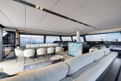 A modern and spacious interior with a large sectional sofa, chairs, and a bar area overlooking a scenic view through the large windows.