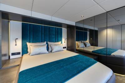 A modern and luxurious bedroom with a large bed, plush teal-colored bedding, and mirrored walls that create a sense of depth and spaciousness.