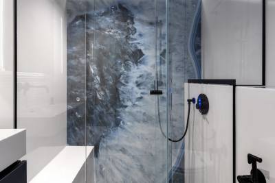 A modern bathroom with a large, glass-enclosed shower featuring a striking, abstract mural-like design in shades of blue and gray, complemented by a minimalist white vanity and fixtures.