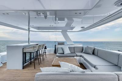 A spacious and modern outdoor deck on a boat, with comfortable seating arrangements, a bar, and a scenic view of the ocean in the background.