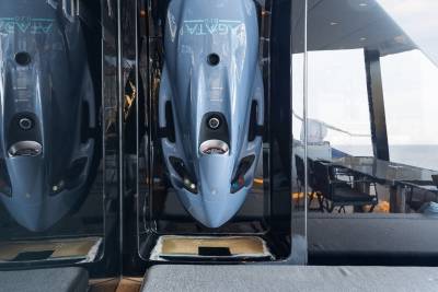 The image shows the front view of two sleek, silver-colored aircraft models or replicas displayed in a glass enclosure, with a blurred background suggesting an indoor setting.