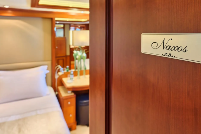 A polished wooden door displays a sign for "Naxos" as a glimpse into a cozy cabin reveals a neatly made bed.