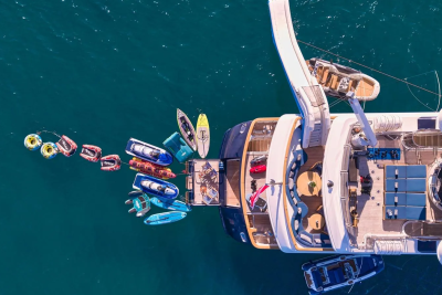 A luxurious yacht is surrounded by an array of water toys, from jet skis to inflatable tubes, ready for adventure on the turquoise sea.