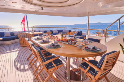 A beautifully set dining table awaits guests on a yacht's deck, overlooking the sparkling blue sea.