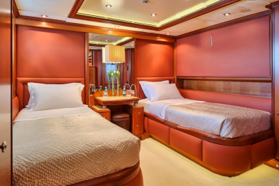Luxurious twin beds with plush white linens and quilted covers are set against warm, coral-toned walls in this elegant stateroom.
