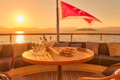 A Turkish flag waves over a yacht's deck as the sun sets, casting a warm glow on a table set for a luxurious meal.