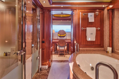 Luxurious wooden paneling and marble accents create an opulent bathroom with a soaking tub and a vanity area overlooking the sea.