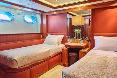 Luxurious twin beds with crisp white linens are bathed in the warm glow of ambient lighting aboard this opulent yacht.