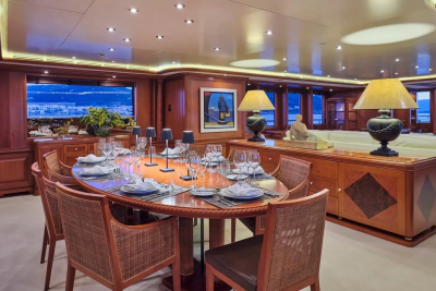 A luxurious yacht dining room is set for an elegant meal with a view of a coastal city at dusk.