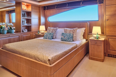 Luxurious wood-paneled yacht cabin features a comfortable bed, elegant decor, and a large window with ocean views.