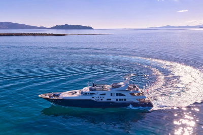 A luxurious yacht carves a white wake through the sparkling blue waters of a serene bay.