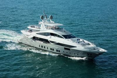 A large, luxurious yacht is sailing across the calm, blue waters of the ocean, leaving a wake behind it.