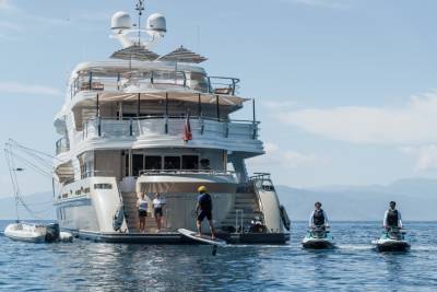 A person on a hydrofoil enjoys the water near a luxurious yacht while two jet skiers follow behind.